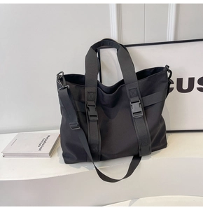 Detail of a black large capacity canvas tote bag with buckles on a minimalist backdrop