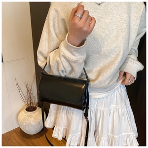 Minimalistische zwarte lakleren tas gestyled met een moderne casual damesoutfit