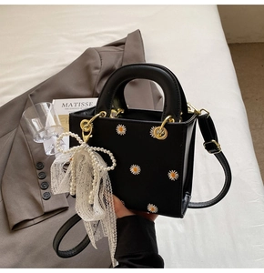 Detail of black daisy handbag featuring pearl bow lace charm and gold hardware