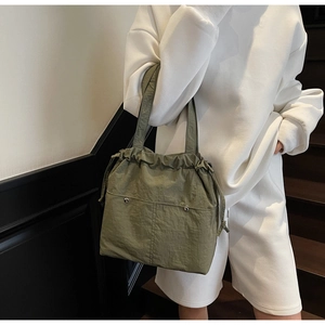 Detail of army green nylon bucket bag with drawstring closure and metal button pocket