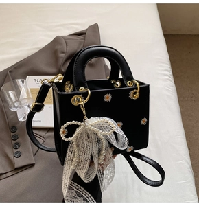 Detail of black tote with daisy embroidery, lace pearl bow, and gold hardware ring handle