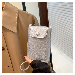 Detail of silver pebble grain leather mini crossbody bag held by hand against a trench coat