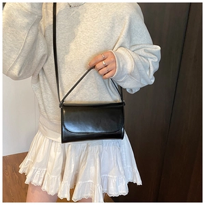 Detail van minimalistische zwarte vierkante lederen tas met schouderriem op plooirok
