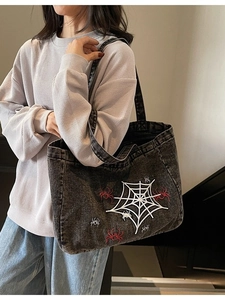 Black denim tote bag with spider web embroidery shown on a model in a stairwell