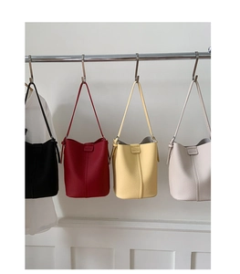 Row of leather bucket bags in black red yellow and white colors hanging on a rack