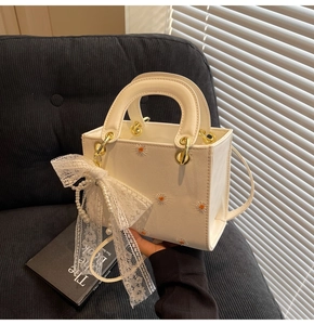 Close-up of white crossbody bag featuring daisy embroidery and a lace pearl bow charm