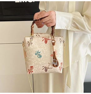 Close-up of bamboo handle and gold chain on beige handbag with goldfish embroidery