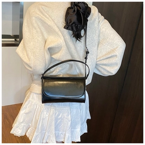 Achteraanzicht van een model met de zwarte glanzende crossbodytas en een witte rok