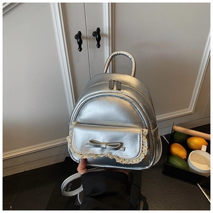 Detail eines silbernen Metallic-Mini-Rucksacks mit Schleife und Spitze in der Hand