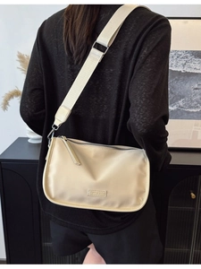 Sac bandoulière minimaliste en nylon beige avec large sangle en toile porté par un mannequin