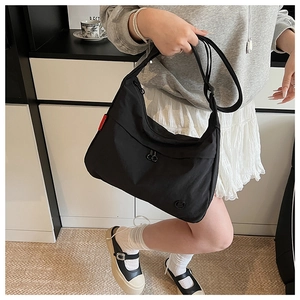 Detail of black nylon half-moon crossbody bag showing front double zippers and red side label