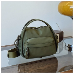 Detail of olive green nylon crossbody bag with wide strap and silver-tone metal zippers