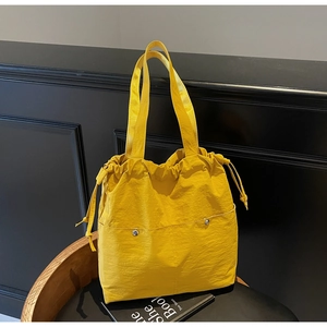 Detail of yellow nylon tote bag featuring drawstring closure and front snap pockets