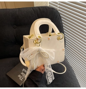 Detail of cream daisy embroidery on bag with lace bow and pearl charm accents