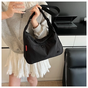 Detail of a large black nylon crossbody bag shown in a daily office commute setting