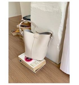 Detail of light beige bucket bag showing litchi grain texture and embossed handle design