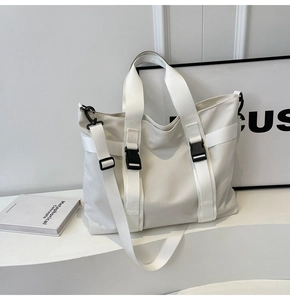 Detailed view of large white canvas tote bag with black buckle straps on minimalist display
