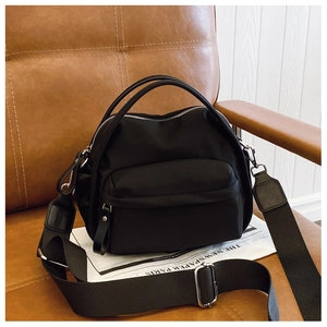 Detail view of a black nylon crossbody bag on a leather chair with a newspaper prop