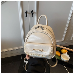Detail eines cremeweißen Mini-Rucksacks mit Spitzenbesatz und stilvoller Schleifenschleife