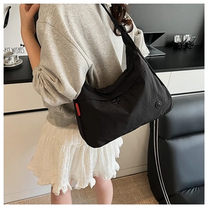 Detail showing the large black nylon crossbody bag with silver zippers and red side label