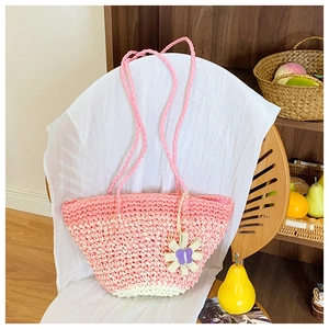 Detail of pink gradient straw shoulder bag with flower charm on a wooden chair