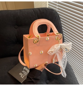 Detail of pink embroidered square bag with white daisy patterns and lace bow accessory