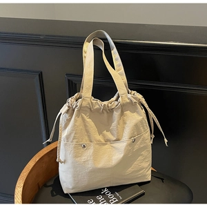 Detailed view of beige nylon drawstring tote bag with front pockets and metallic rivets