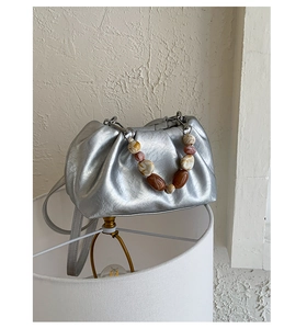 Detail of silver pleated pouch bag featuring multi-color beaded handle and sleek strap