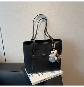 Detail der schwarzen Tragetasche mit Lederstruktur und niedlichem Teddybär-Anhänger