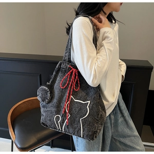 Detail of large denim tote bag featuring white cat embroidery and red woven rope accent