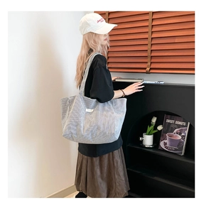 Grand sac cabas en toile rayée grise porté à l'épaule dans un intérieur minimaliste