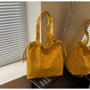 Detail of yellow nylon tote bag featuring drawstrings and metal snap front pockets