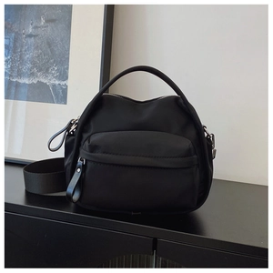 Detail of minimalist black nylon crossbody bag featuring silver hardware and a wide strap