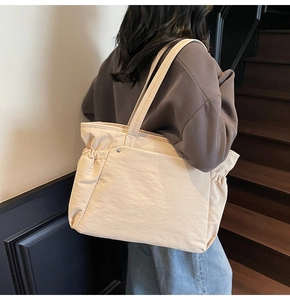 Détail d'un grand sac cabas en nylon beige porté par un mannequin dans un escalier