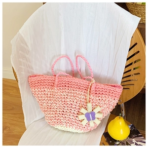 Detail of pink gradient woven straw bag with floral charm on a rustic wooden chair