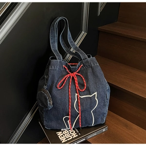 Detail of blue denim drawstring tote bag with cat embroidery and red woven rope handles