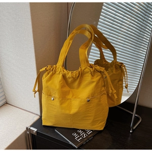 Detail of bright yellow tote bag with drawstring closure and silver buckles on front pockets