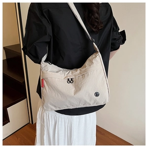 Detail of cream nylon crossbody bag featuring red side label and black round logo emblem
