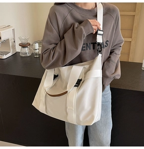 Large white canvas tote bag with brown leather accents and adjustable straps shown on model