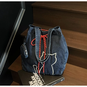 Detail of blue denim tote bag with white cat embroidery and red drawstring on wooden stairs