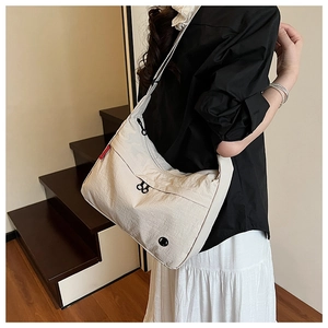 Detail of a beige nylon crossbody bag featuring a front zipper pocket and wide shoulder strap