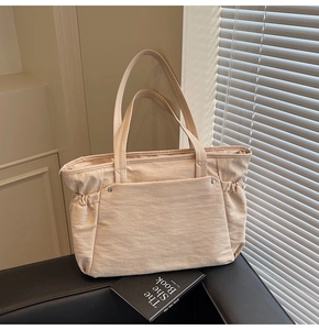 Détail d'un grand sac cabas beige avec cordons latéraux et poche sur un siège en cuir