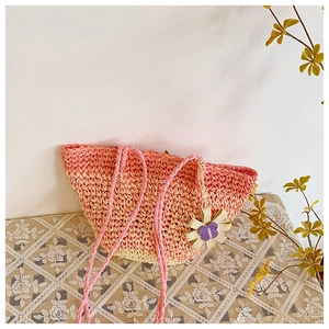 Detail of handmade gradient straw tote bag with delicate floral pendant on a lace table