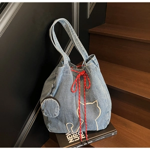Detail view of light blue denim tote bag with cat embroidery and striped drawstring