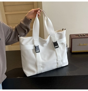 Detail of white canvas tote bag featuring buckle straps and functional nylon handles