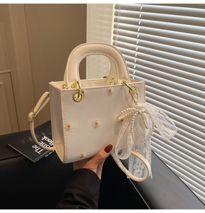 Close-up of white crossbody bag with daisy embroidery and pearl bow accessory