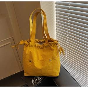 Detail view of bright yellow tote bag with drawstring closure and metal rivet accents