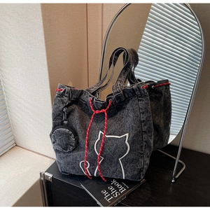Detail of black denim tote bag with cat embroidery and red drawstring cord accents