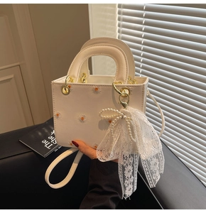 Detail of cream handbag with daisy embroidery and lace pearl bow charm detail