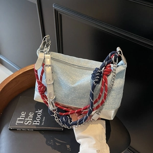 Close-up of light blue denim tote with silver studs, metal chain and woven rope detail